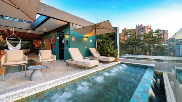 A rooftop pool area with lounge chairs and umbrellas, a view of the cityscape, and a glass-enclosed section.