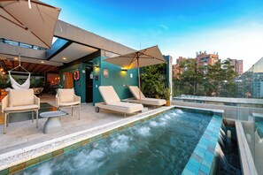 A rooftop pool area with lounge chairs and umbrellas, a view of the cityscape, and a glass-enclosed section. - Hotel Celestino Boutique (Medellín)