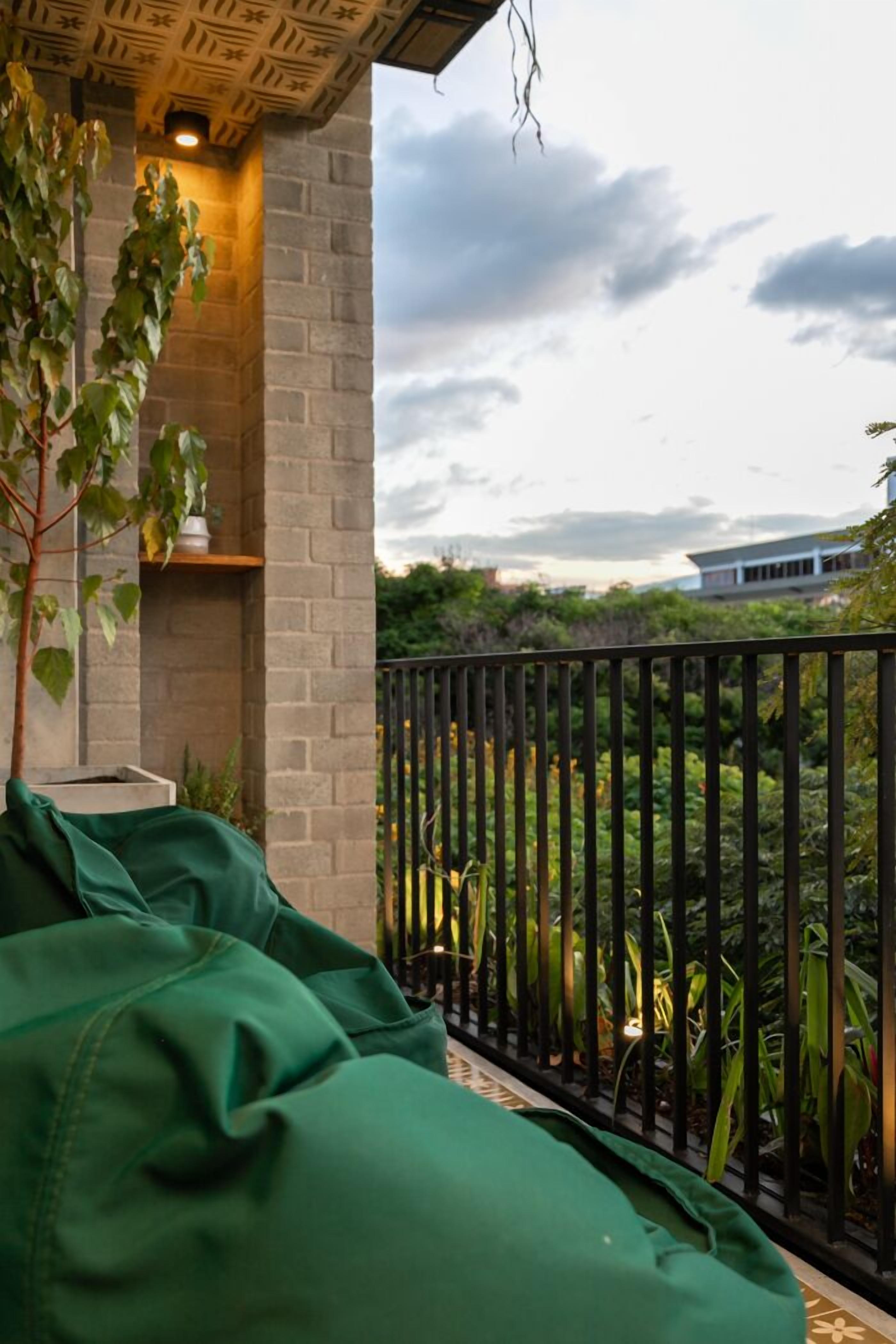A balcony with a green sofa, a potted plant, and a brick wall.