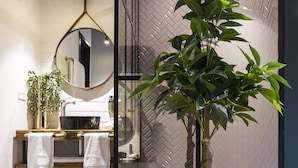 A modern bathroom with a wooden floor, a round mirror, a sink with a gold faucet, and a potted plant.