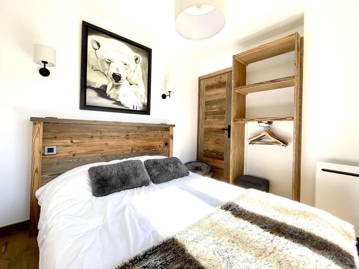 A bedroom with a wooden headboard, a white bedspread, a polar bear painting, and a wooden wardrobe.