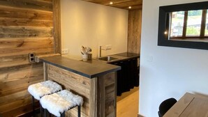 A kitchen with wooden walls, a central island with stools, a window with a view, and a sink. - 50m from ski slopes, 3rd floor, swimming pool, sauna, hammam, balcony, tv, ski locker, 55m² (Champagny-en-Vanoise)