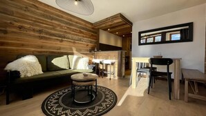 A modern living room with a wooden accent wall, a round coffee table, a sofa, and a dining area with chairs and a table. - 50m from ski slopes, 3rd floor, swimming pool, sauna, hammam, balcony, tv, ski locker, 55m² (Champagny-en-Vanoise)