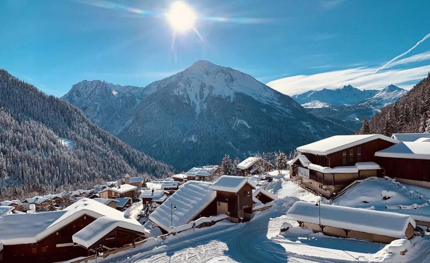 Ein verschneites Bergdorf mit Chalets, einem klaren Himmel und einem markanten Berggipfel im Hintergrund.