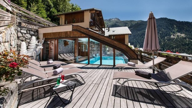 Une terrasse en bois avec des chaises longues et une piscine, offrant une vue sur un paysage montagneux.