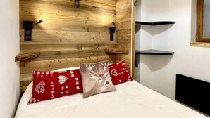 Une chambre à coucher avec une tête de lit en bois, un lit recouvert de draps blancs, des oreillers à motifs rouges et blancs, et une tête de cerf accrochée au mur.