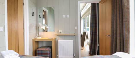 A bedroom with two beds, a bedside table with a lamp, a radiator, and a mirror on the wall.