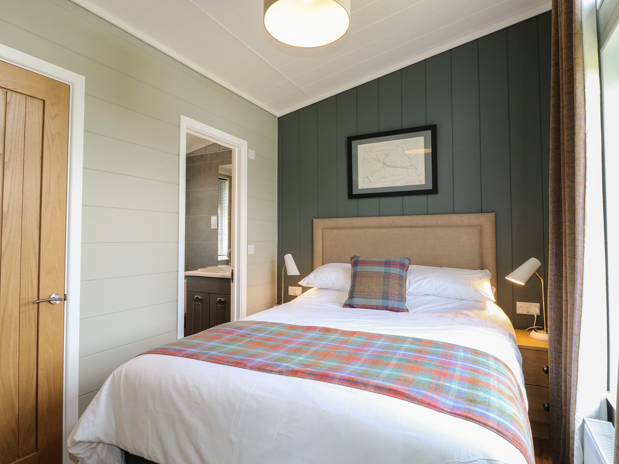A bedroom with a bed, nightstands, a framed map on the wall, and a door to a bathroom.
