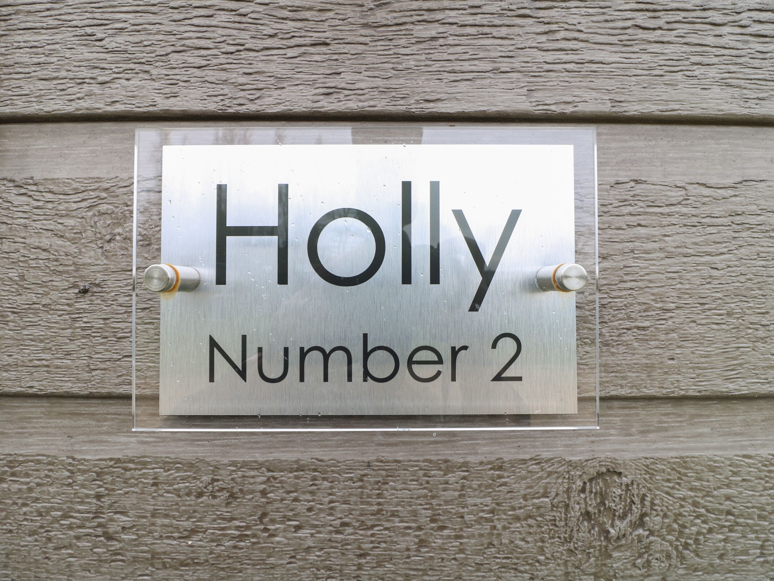 A metal sign with the name "Holly" and the number "2" mounted on a textured wall.
