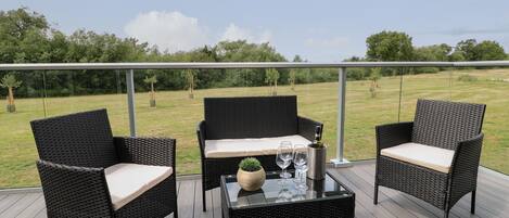 A balcony with wicker furniture, a glass table, and a bottle of wine.