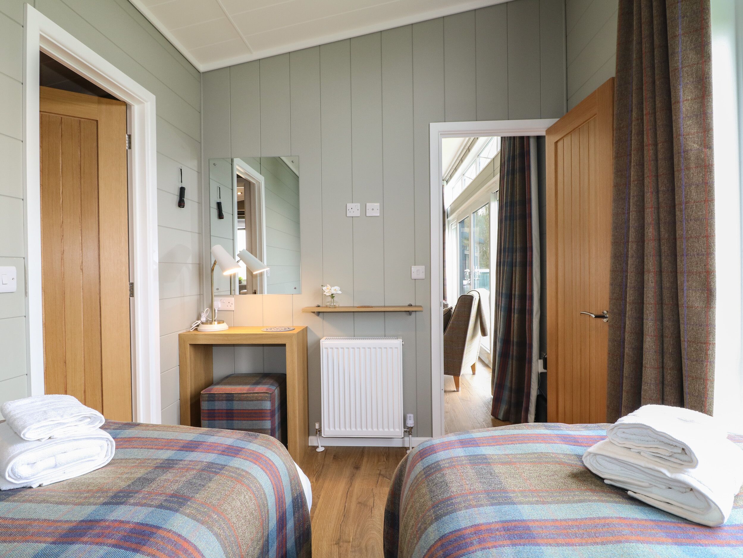 A bedroom with two beds, a bedside table with a lamp, a radiator, and a mirror on the wall.