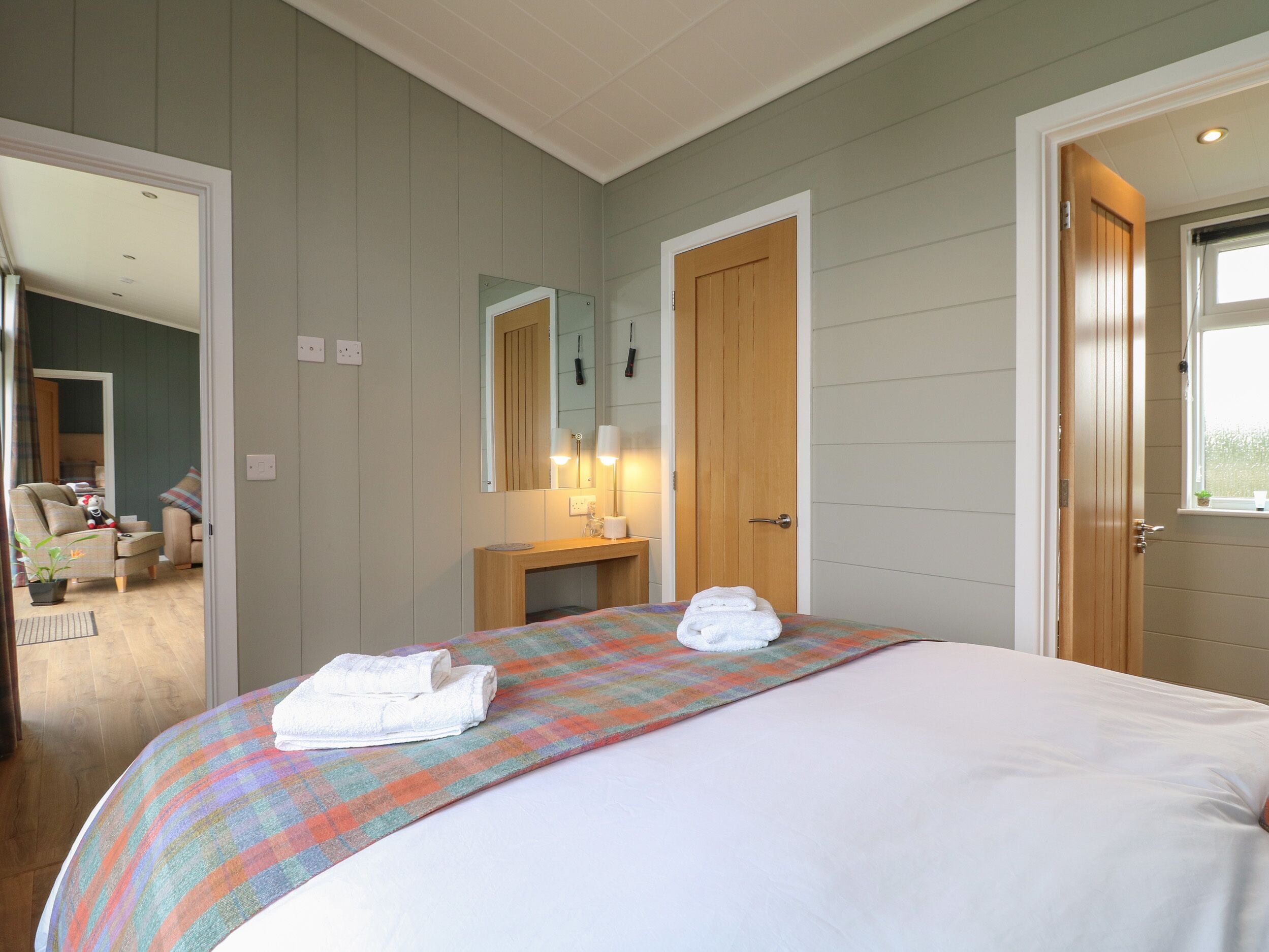 Une chambre à coucher avec un lit, une table de chevet avec une lampe, un miroir et une porte donnant sur une autre pièce.