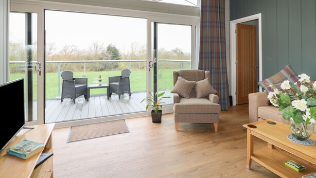 A spacious living room with a large sliding glass door leading to an outdoor patio area. - Cedar Lodge (Newark)