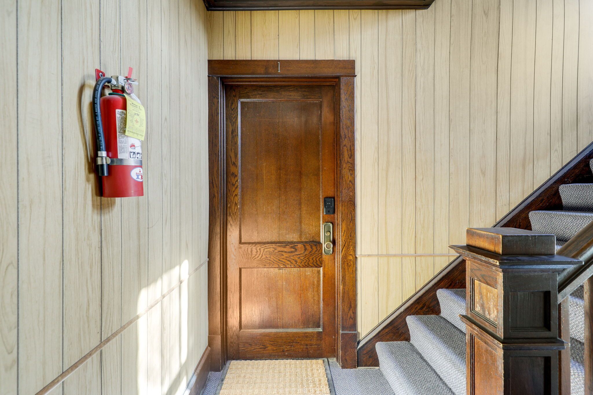 A wooden door with a fire extinguisher mounted on the wall to its left.