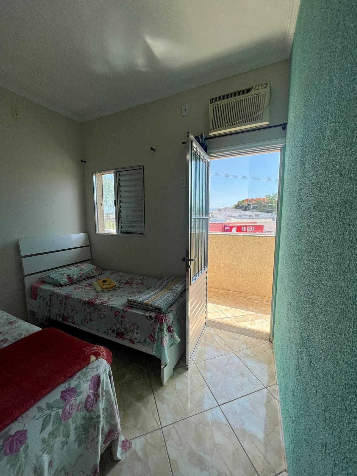 A bedroom with two beds, a window, an air conditioning unit, and a view of a building outside.