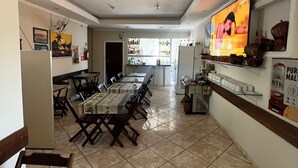 A spacious dining area with a long table and chairs, a television mounted on the wall, and a kitchen area visible in the background. - Hotel e Restaurante Roseira (Roseira)