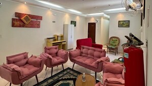 A living room with four pink armchairs, a coffee table, and a patterned rug. There is a red fire extinguisher on the wall and a door leading to another room. - Hotel e Restaurante Roseira (Roseira)