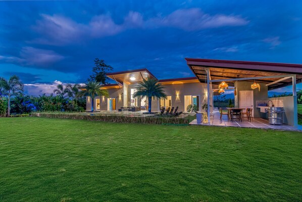 A modern house with a covered patio, outdoor seating, and a well-maintained lawn. - Mayoli Hill Deluxe Farmhouse Hot Tub & Private Pool with Volcano View (Alajuela Province)