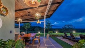 Eine Terrasse im Freien mit einem Holztisch und Stühlen, umgeben von Blumentöpfen und Blick auf die Landschaft.