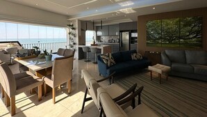 A modern living room with a dining area, kitchen, and large windows overlooking the sea. - Apartamento Astúrias (Guarujá)