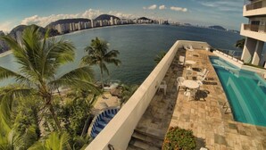 A rooftop pool area with a view of the ocean and city skyline. - Apartamento Astúrias (Guarujá)