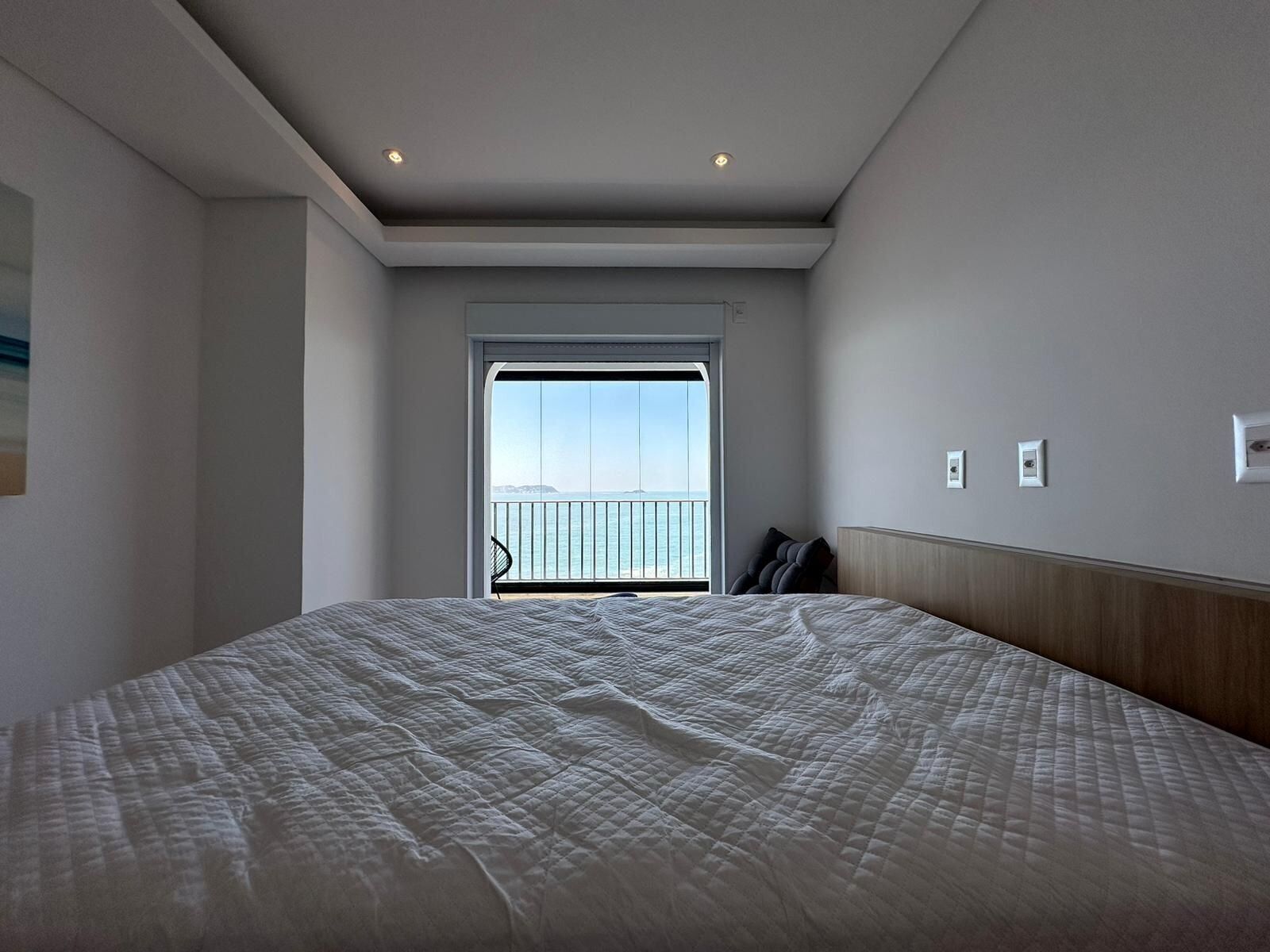 A hotel room with a large bed, a view of the sea through a balcony, and a modern design.