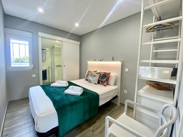 A modern hotel room with a bed, a shower, a wardrobe, and a small seating area.