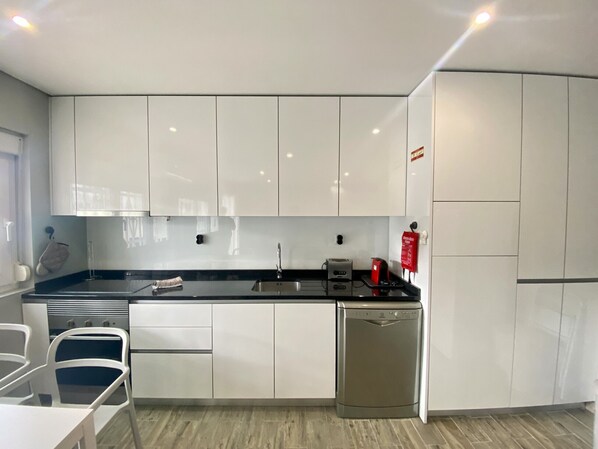 A modern kitchen with white cabinets, a black countertop, a dishwasher, and a coffee maker.