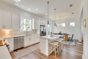 A modern kitchen with white cabinetry, a central island with stools, a dining area with a wooden table, and pendant lighting.