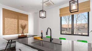 A modern kitchen with a large island, black faucet, and a view of the outside through a window. - Pura Vida House - 2 King Bed - Entire Home (Sacramento)