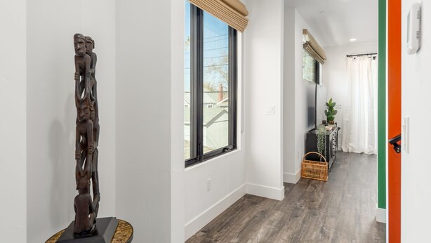 A hallway with a wooden sculpture, a large window with blinds, a basket, and a plant on a table. - Pura Vida House - 2 King Bed - Entire Home (Sacramento)