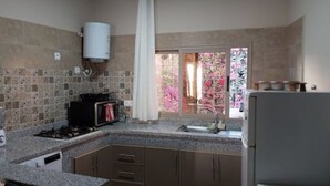 A kitchen with granite countertops, a gas stove, a refrigerator, and a window with a view of pink flowers.
