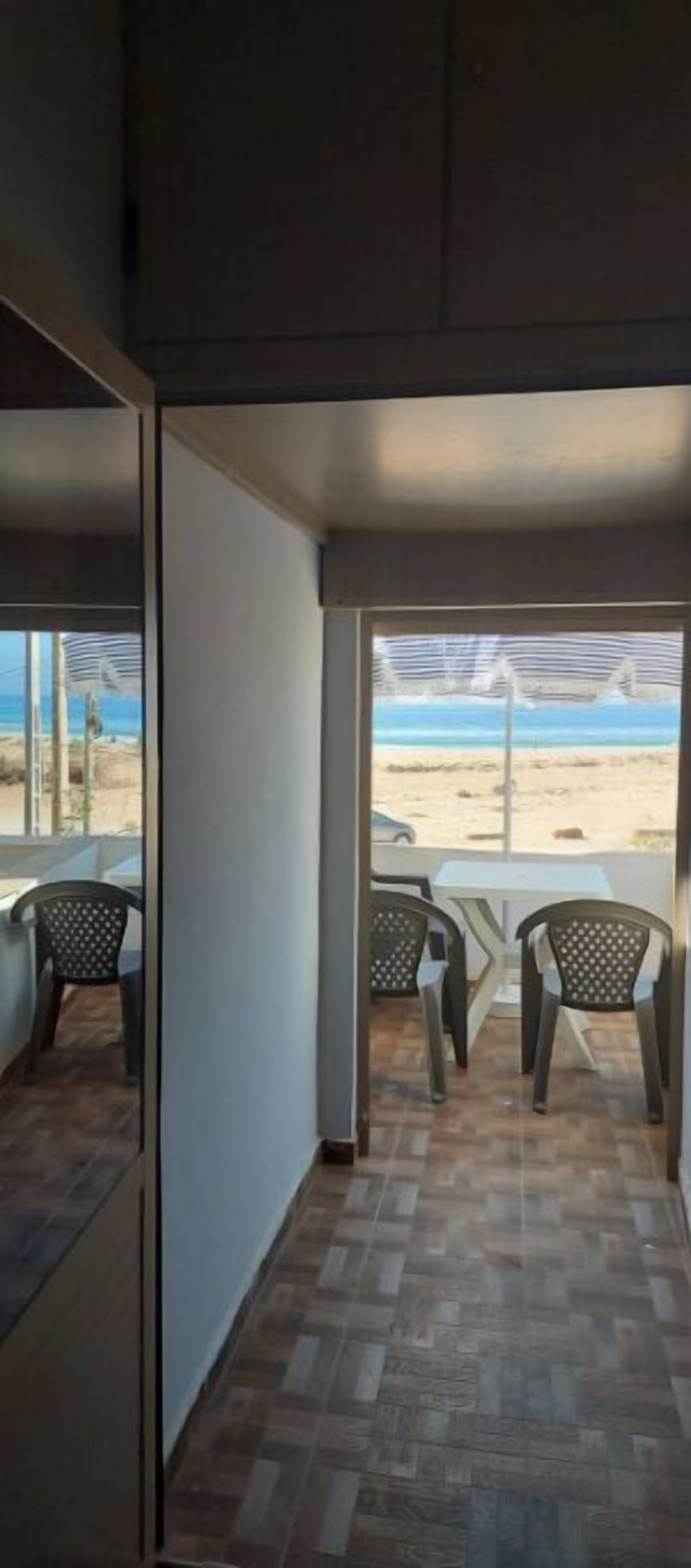 A room with a view of the beach, a small table, and two chairs.