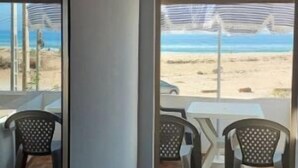 A room with a view of the beach, a small table, and two chairs.