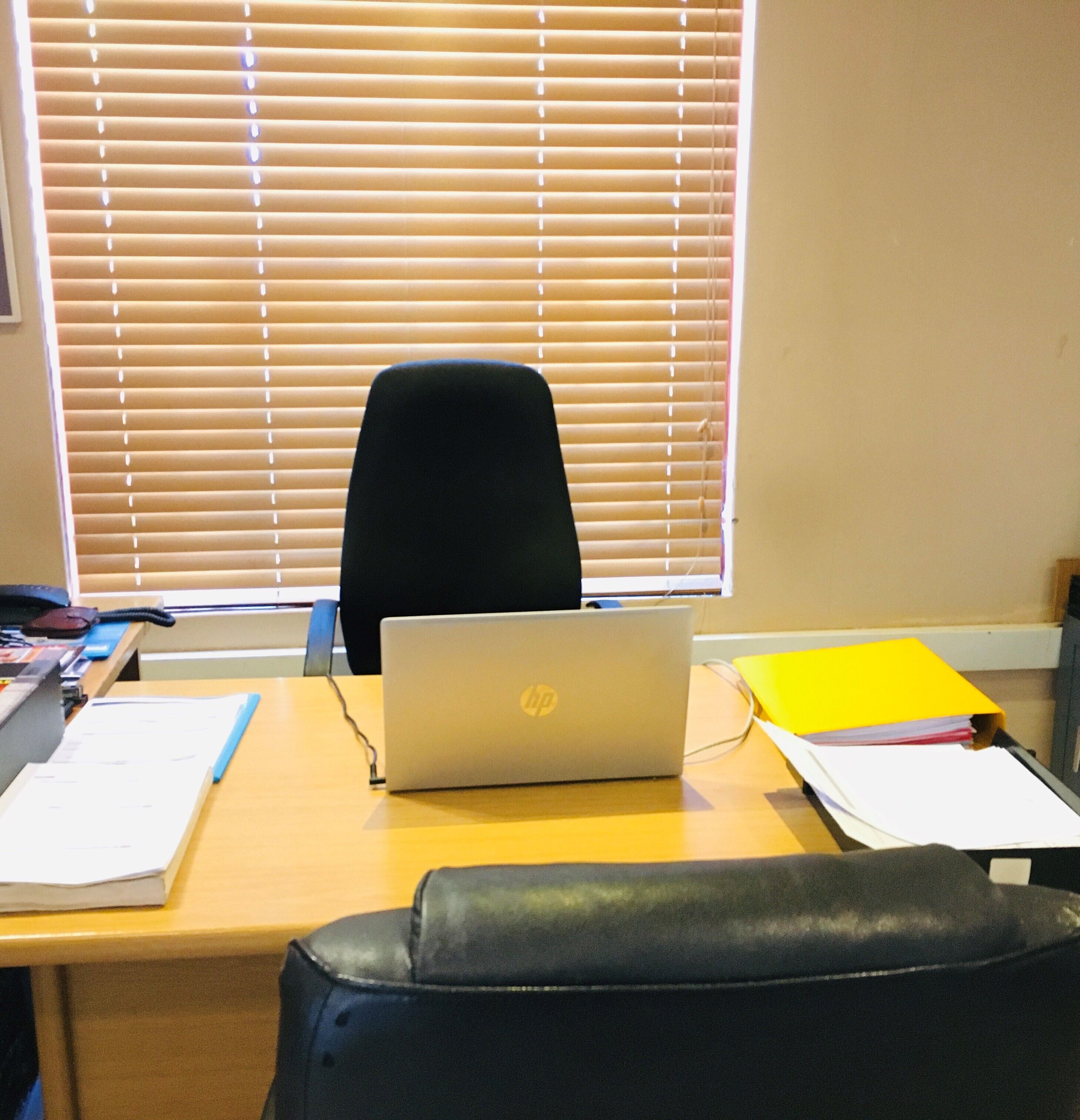 Un bureau avec un ordinateur portable HP, une chaise de bureau noire et une fenêtre avec des stores.