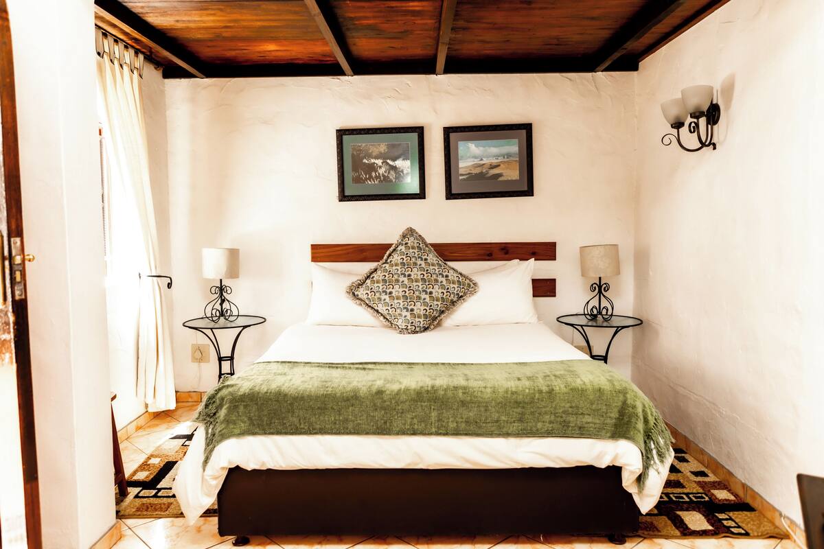 Ein Schlafzimmer mit einem Bett, zwei Nachttischen, einer grünen Tagesdecke und zwei gerahmten Bildern an der Wand.