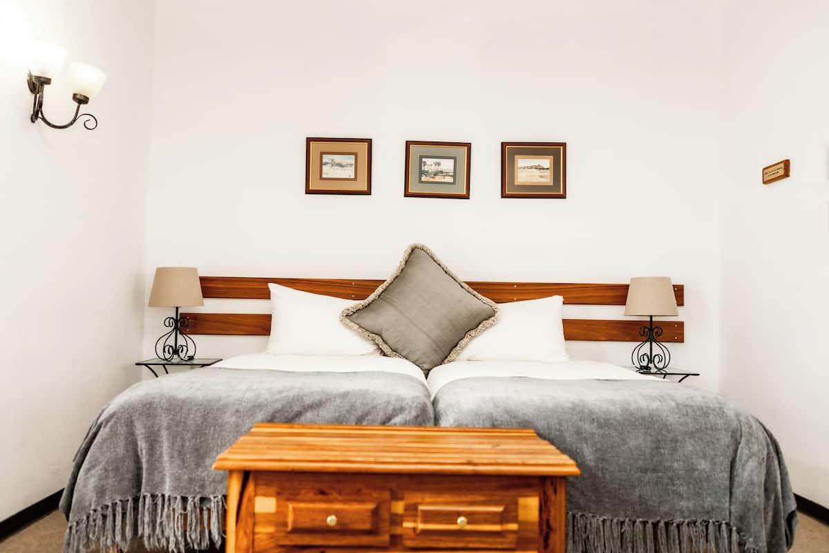 Ein Doppelbett mit Holz Kopfteil, zwei Nachttische mit Lampen, ein kleiner Holznachtisch und drei gerahmte Bilder an der Wand.
