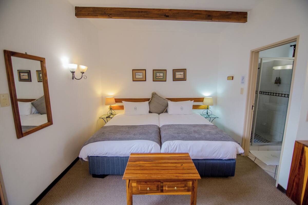 Ein Doppelbett mit Holz-Kopfteil, Nachttischlampen und einem kleinen Holztisch in einem Hotelzimmer.