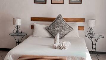 A bedroom with a large bed, wooden bench, chandelier, framed pictures, and two bedside tables with lamps.