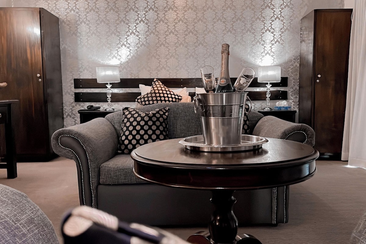A modern living room with a grey sofa, a round coffee table with a champagne bucket, and a patterned wallpaper background.