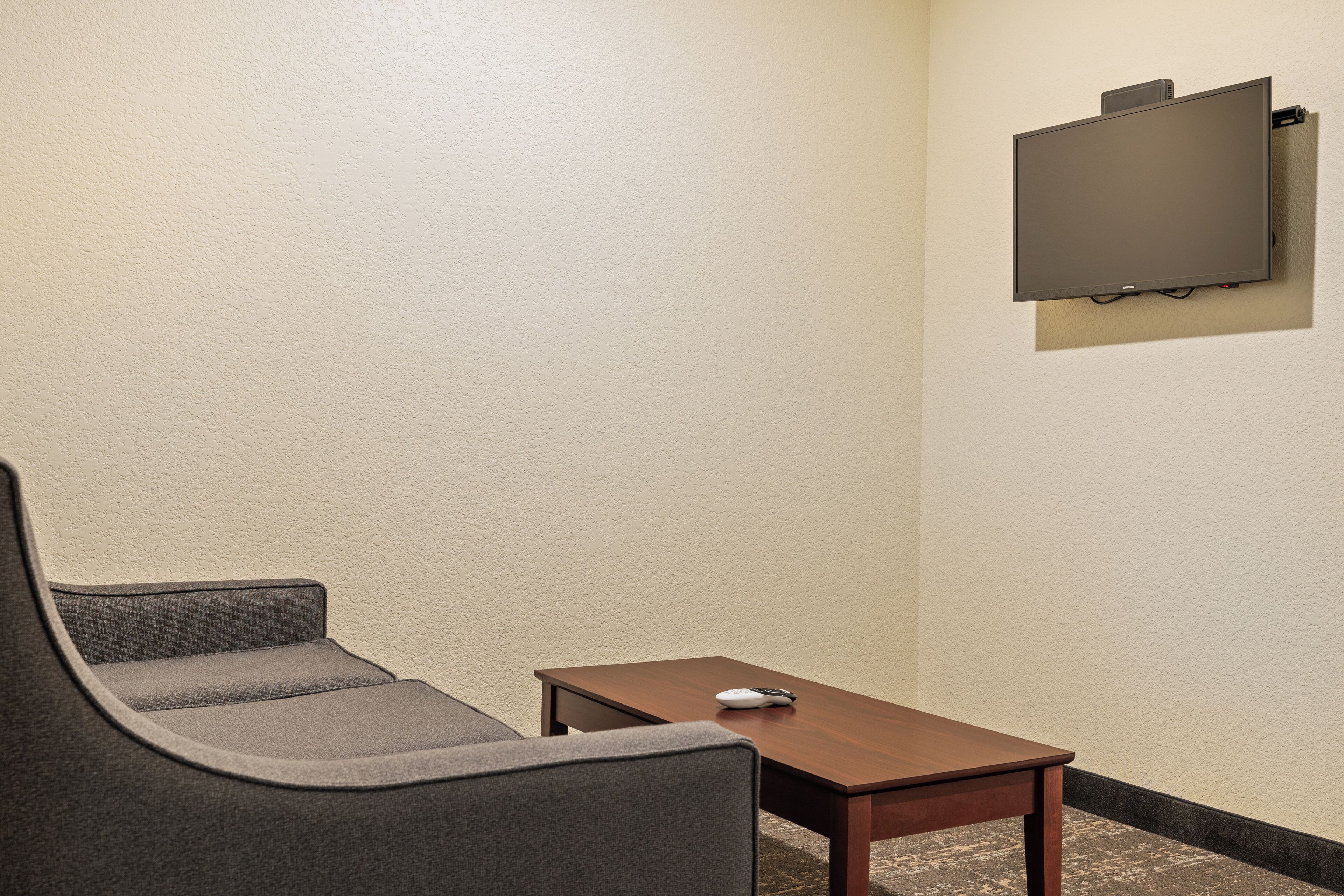A small, private room with a single gray chair, a wooden table, and a mounted flat-screen TV.