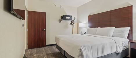Habitación de hotel con cama, mesita de noche, lámpara, estante en la pared y una puerta.