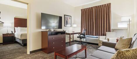 Habitación de hotel con cama, escritorio, televisor, cómoda, sofá y ventana con cortinas.
