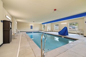 Una piscina interior con agua cristalina, una escalera de metal y varias sillas de descanso alrededor de la zona de la piscina.