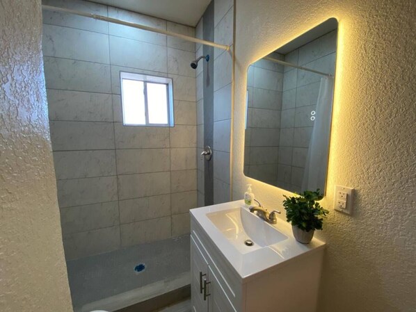 Een badkamer met een douche, wastafel, spiegel en raam.