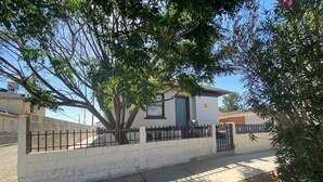 Un pequeño edificio de una sola planta con fachada blanca y techo oscuro, rodeado por una cerca de metal negro.