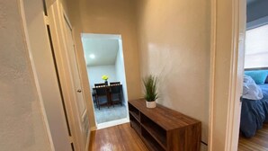 Un pasillo con suelo de madera, una pequeña mesa con sillas y una planta en maceta.