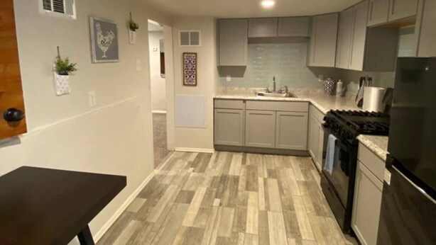 Una cocina moderna con armarios grises, un refrigerador negro y piso de madera.