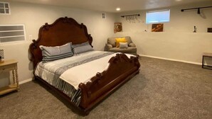 Un dormitorio con cama de madera, alfombra gris, una mesita y una ventana con persianas.
