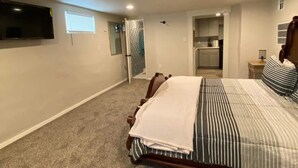 Un dormitorio con cama, televisor montado en la pared, kitchenette pequeño y baño con ducha.